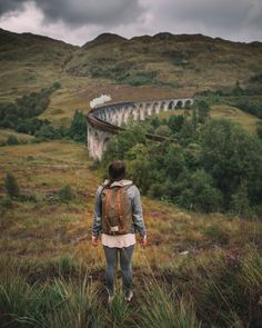 a person with a backpack standing in front of a train on the side of a hill