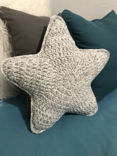 a crocheted star pillow sitting on top of a bed next to two pillows