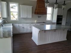 a large kitchen with white cabinets and marble counter tops, an island in the middle