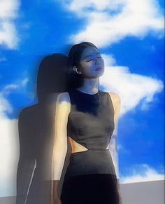 a woman is standing in front of a blue sky with clouds and her shadow on the wall