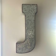 the letter j is made out of metal and sits on a white wall next to a window