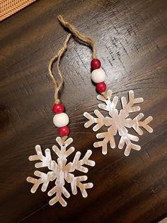 two snowflakes are hanging on a wooden table with beads and red berries