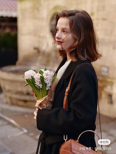 a woman is walking down the street with flowers in her hand and holding a purse