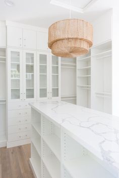 a white kitchen with marble counter tops and cabinets in the center, hanging light fixture above it