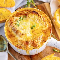 a casserole dish with cheese and herbs in it on a wooden cutting board