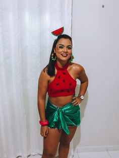 a woman in a red top and green skirt standing next to a white wall with a watermelon on it