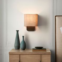 two green vases sitting on top of a wooden dresser next to a wall light