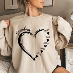 a woman sitting on a bed wearing a sweatshirt with the words grandma and hearts printed on it