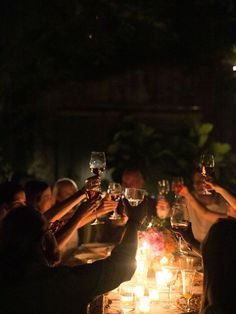 a group of people toasting wine glasses at a dinner table with candles on it