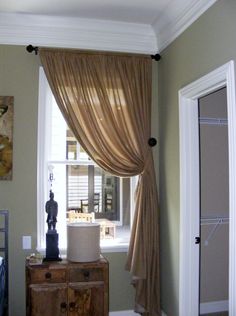 a living room with a large window and drapes on the windowsill, next to a dresser