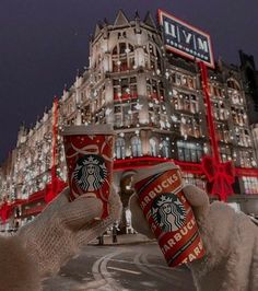 two stuffed animals holding up starbucks cups in front of a building with lights on it