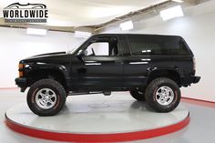 a black truck is parked in a large room with white walls and red flooring