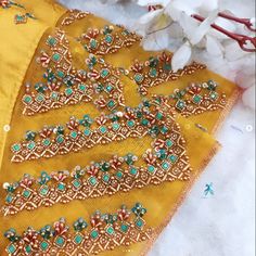 an embroidered yellow saree with green and blue beads on it, next to flowers