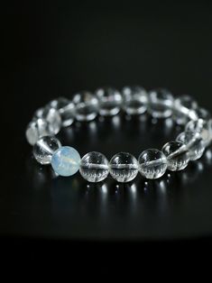 a bracelet made out of clear glass beads on a black surface with a light blue bead