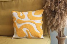 a yellow and white pillow sitting on top of a couch next to a tall plant