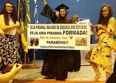 three women in graduation gowns holding up a sign