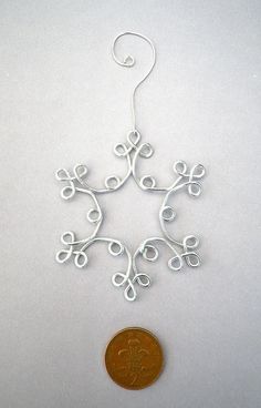 a penny sitting next to a wire snowflake ornament on a white surface