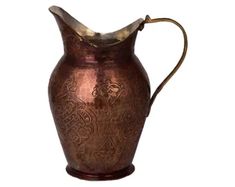 an antique copper pitcher with ornate designs on the bottom and handle, is shown against a white background