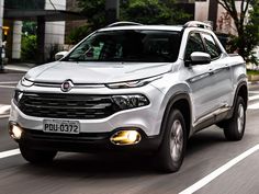 the front end of a white suv driving down a street with buildings in the background