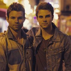 two young men standing next to each other in front of a street light at night