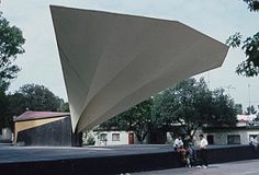 people are standing in front of a large triangular structure on the side of a road