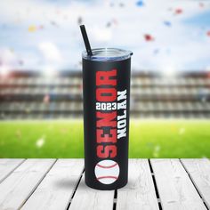 a black tumbler cup with a red and white baseball on it sitting on top of a wooden table