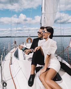 a man and woman sitting on the back of a sailboat in the ocean, wearing sunglasses