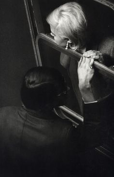 black and white photograph of a woman looking out the window on a train with her hand in her mouth