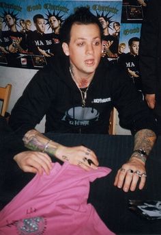 a man sitting at a table with tattoos on his arms and arm, holding onto a pink shirt