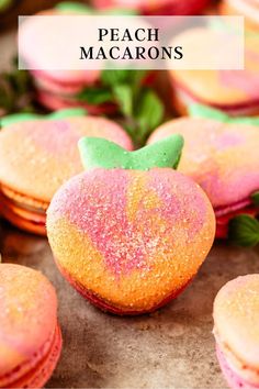 peach macarons with green leaves and powdered sugar on top, in front of other macaroons