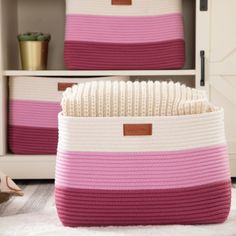 two pink and white storage baskets sitting on top of a rug in front of a bookcase