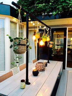 a table with some plants on it and lights hanging from the ceiling over it in front of a house