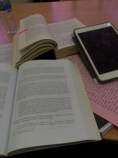 an open book sitting on top of a table next to a smart phone and water bottle