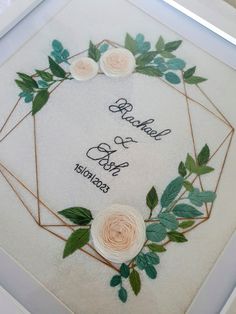 an embroidered wedding card with roses and leaves on the front, in a white frame