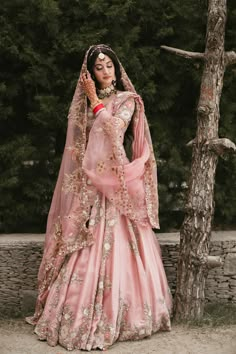 a woman in a pink wedding dress standing next to a tree and wearing a veil