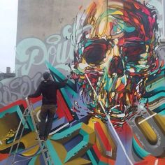 a man is painting a mural on the side of a building in front of a large skull