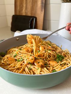 a person is eating pasta with shrimp and parsley in a skillet on the kitchen counter