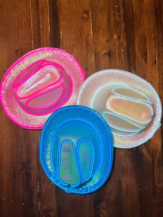 three different colored plates on a wooden table with plastic utensils in the middle