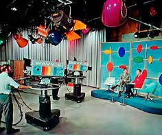 two men are sitting in chairs on the set of an episode with balloons hanging from the ceiling