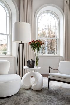 a living room filled with white furniture and large arched windows next to a window covered in curtains