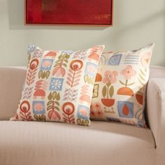 a couch with three pillows on it in front of a red painting and two framed pictures