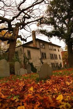 an old house surrounded by trees and leaves on the ground in front of some tombstones