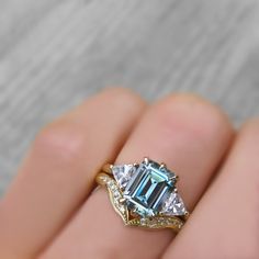 a woman's hand holding a ring with an aqua and white diamond