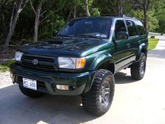 a green truck parked on the side of a road next to some trees and bushes