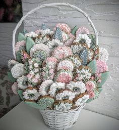 a white basket filled with lots of flowers on top of a wooden table next to a wall