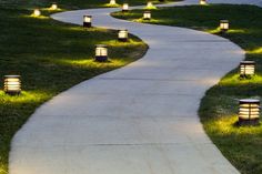 some lights that are sitting on the side of a path in the grass and one is lit up