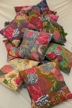 a pile of colorful pillows sitting on top of a white bed next to each other