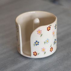 a white cup with flowers painted on it sitting on top of a gray countertop