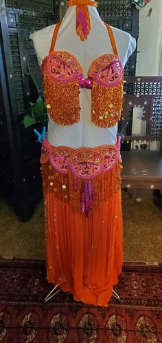 I called this bellydance costume "The Great Pumpkin".  It is in excellent condition. This costume package includes the bra and belt, necklace, earrings, 2 skirts, 2 veils, 2 jackets, harem pants, orange mesh stomach cover, and extras beads for repairs or alterations. The bra is a size 36B. The belt is currently 41in, but can be adjusted smaller or larger.  It is fully lined in orange felt.  The necklace is 14in.  The earrings are for pierced ears. The outer skirt was imported from Egypt.  It is pleated chiffon, each pleat is sequined from top to bottom.  The skirt is 35in long and is slit on one side.  The orange underskirt is chiffon and also 35in long. The harem pants are made of the same fabric as the underskirt.  One jacket is orange satin and ties under the bra. From shoulder to elbow Orange And Hot Pink, Pink Veil, Bellydance Costume, The Great Pumpkin, Orange Chiffon, Great Pumpkin, Orange Satin, Belly Dance Costume, Belly Dance Costumes