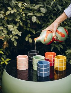 a person pours water from a watering can into colorful cups on top of a table